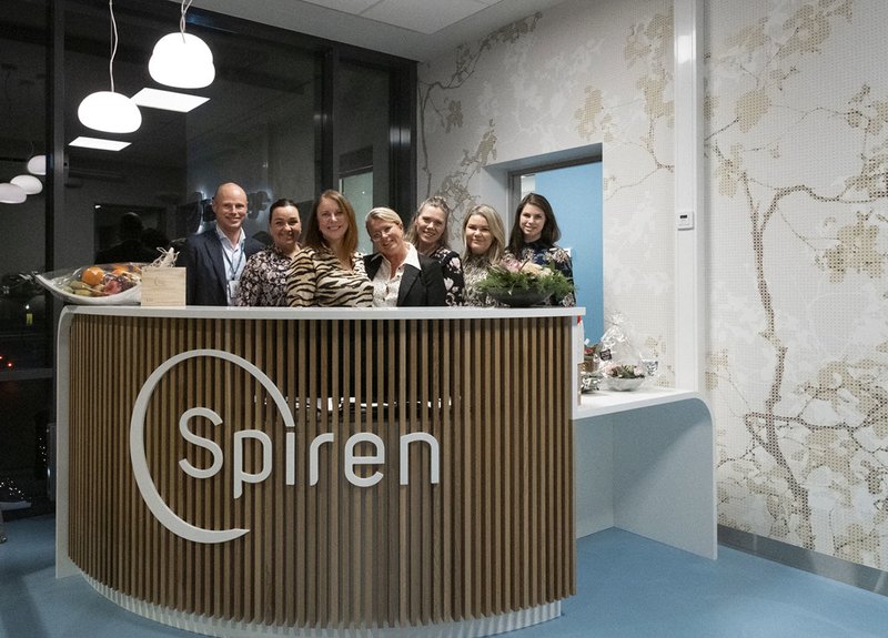 Gruppebilde av alle de ansatte i Spiren Fertilitetsklinikk som står stående bak resepsjonen mens de smiler