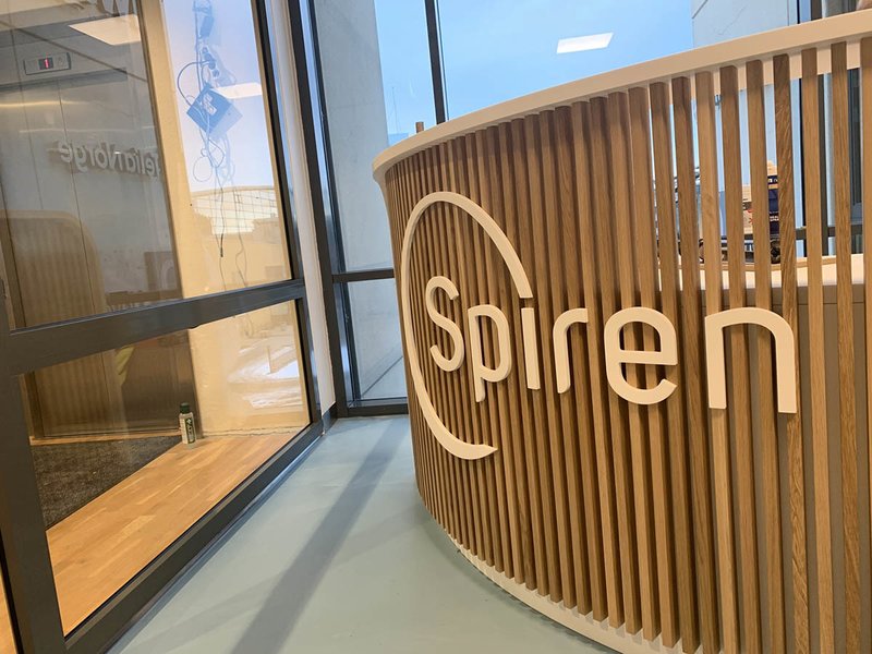 Nærbilde av resepsjonen til Spiren fertilitetsklinikk, logoen til Spiren er synlig på toppen av moderne treverk med gap mellom hver planke som sammen utgjør resepsjonen